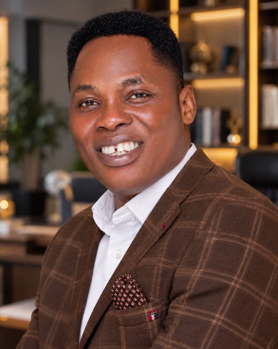 Wole Abraham Martins smiling, in a brown check blazer in his study