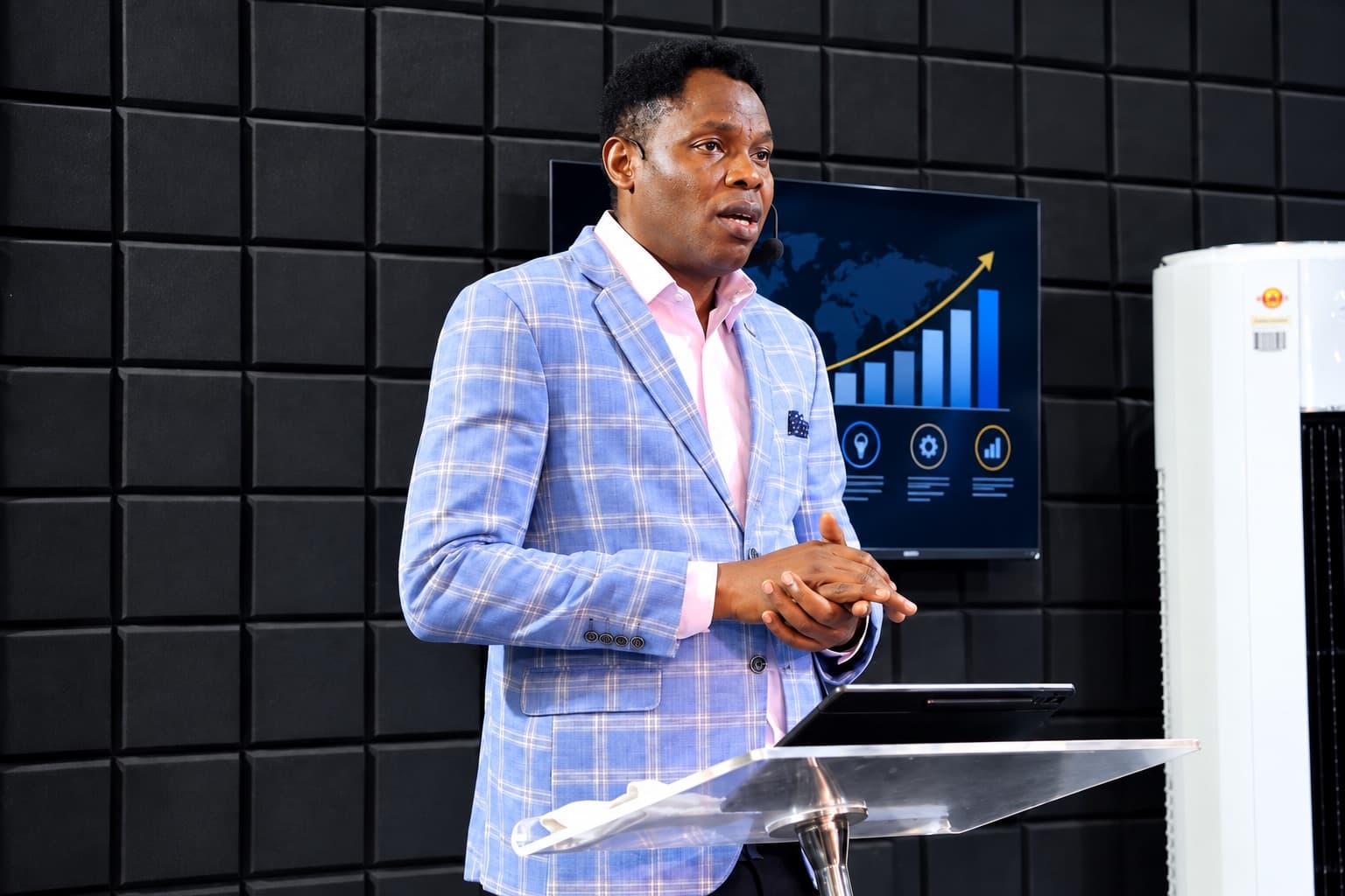 Wole Abraham Martins teaching at a clear lectern, a growth chart on the screen behind him